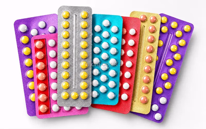 Several blister packs of oral contraceptive pills in different colours fanned out on a white background